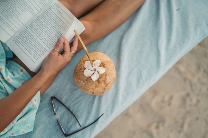 Close-up shot of woman reading a book with coconut drink