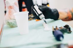 Hands in latex gloves filling tattoo inks in pots