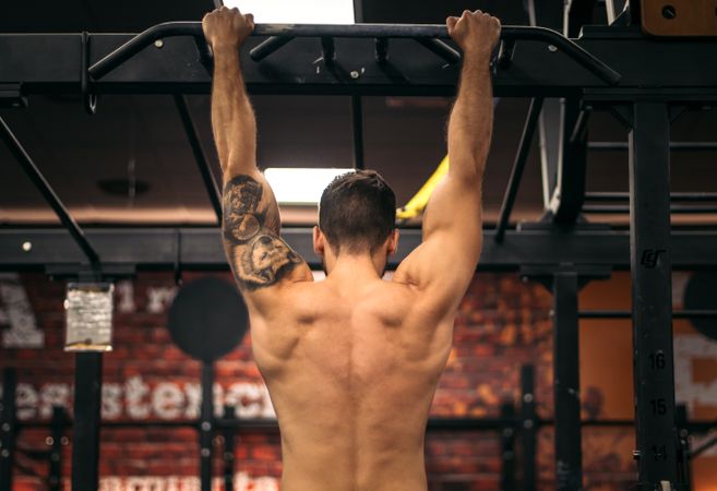 back view of a strong man doing pull ups in a gym