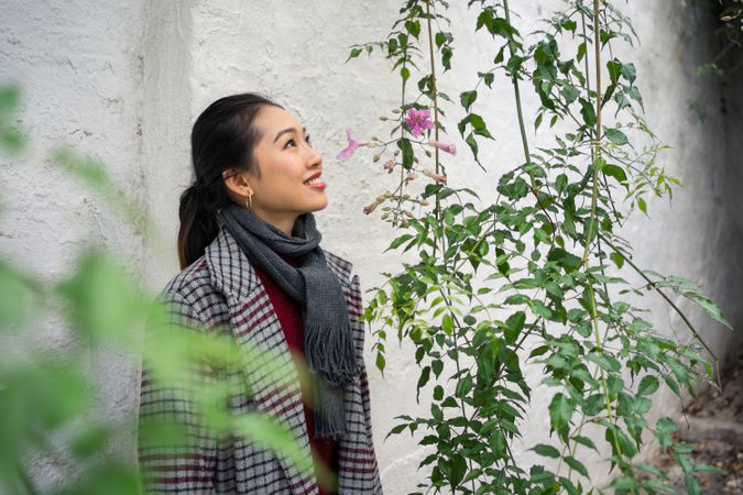 Young female in casual clothing touching green plants and smiling at rocked lane