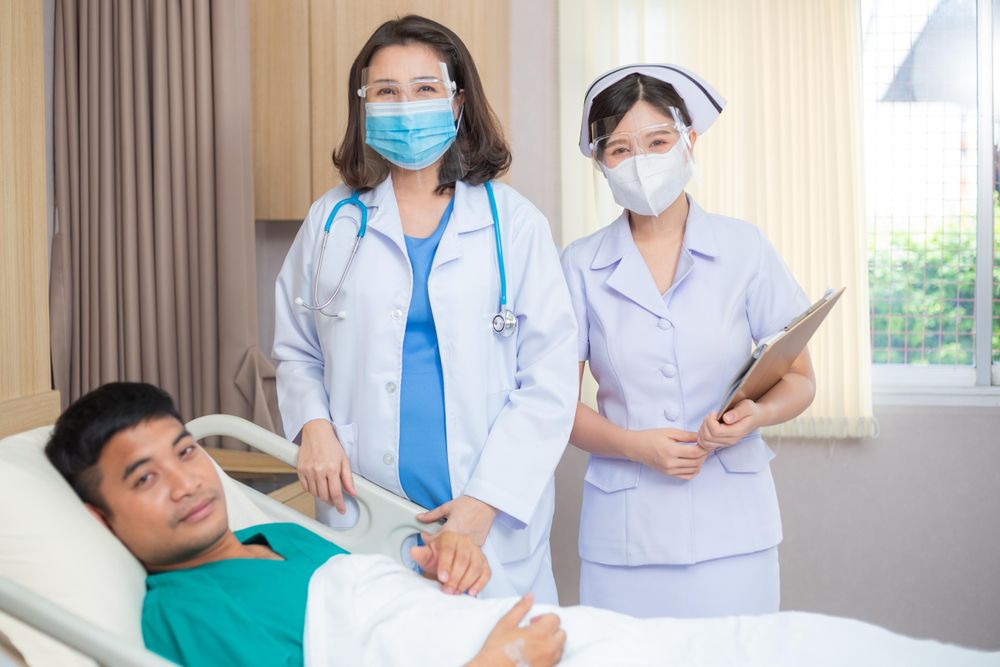 Portrait of two female medical professionals with male patient in hospital bed