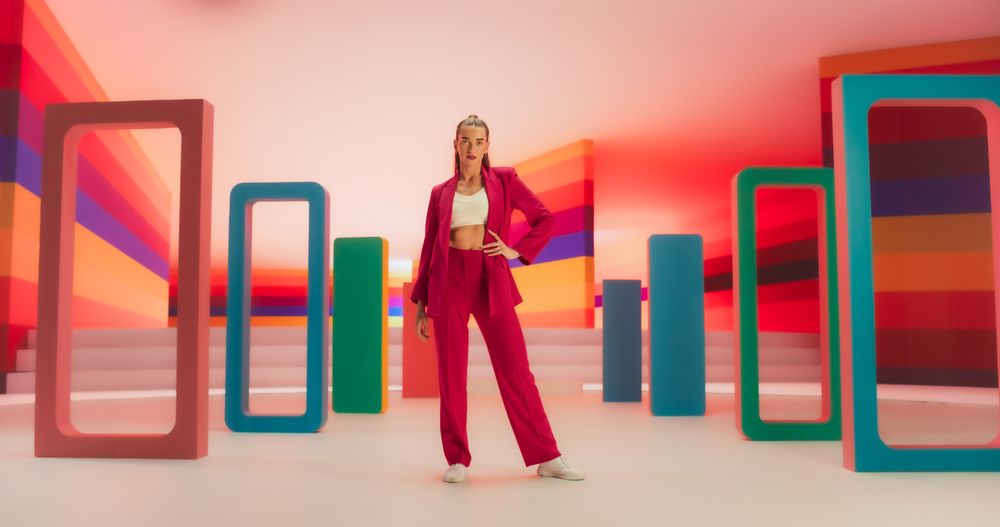 Low Angle Portrait of a Stylish Female Posing Confidently in a Bright Lit Room. Fashionable Young Woman Striking A Pose In Colorful Creative Studio Environment, Working For Luxurious Fashion Brand.