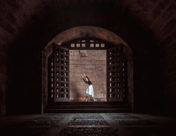 Graceful ballerina dancing in dark passage near stone brick