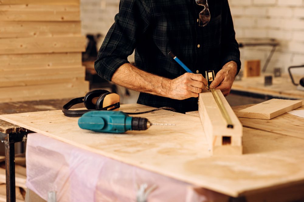Male carpenter measuring wood and marking it with pencil