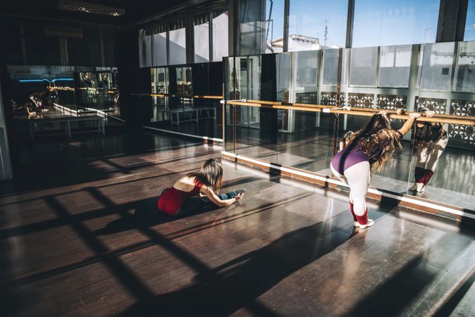 Young ballerinas working out in spacious sunny studio warming up muscles in front of mirror.