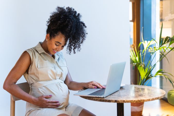 Smiling Black woman touching belly while browsing laptop
