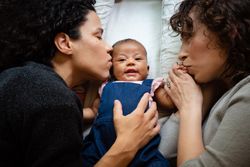 Two mothers kissing their new born