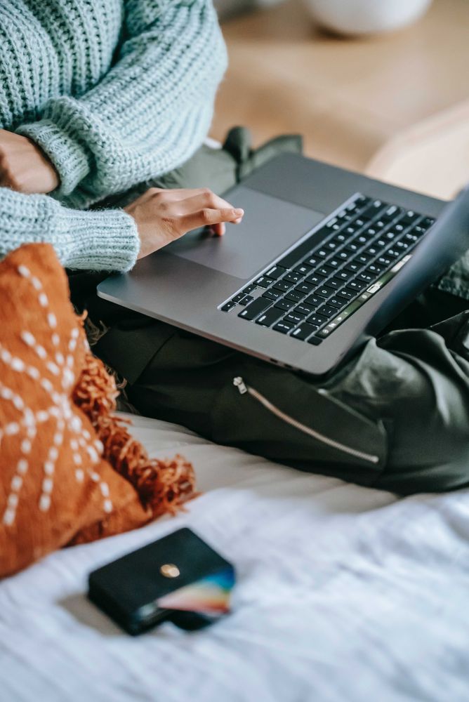 Person in blue knit sweater using laptop in bed