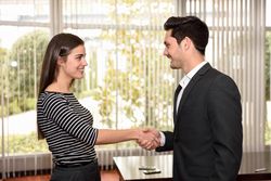 Happy male and female business colleagues shaking hands in front of window