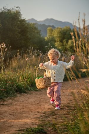 Funny girl with wicker basket waling on countryside road