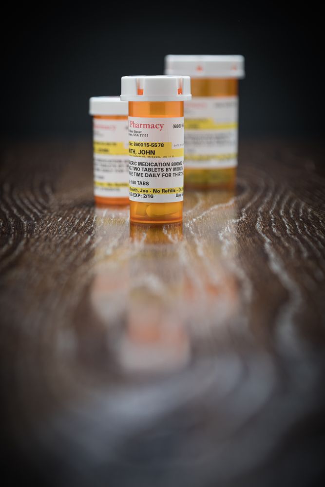 Variety of Non-Proprietary Prescription Medicine Bottles on Reflective Wooden Surface.