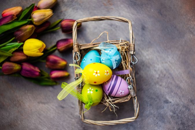 Decorative Easter eggs in basket on table with tulips