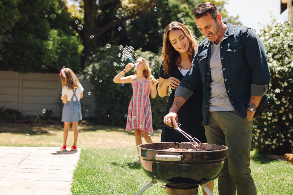 Happy man and woman making BBQ standing together in their backyard