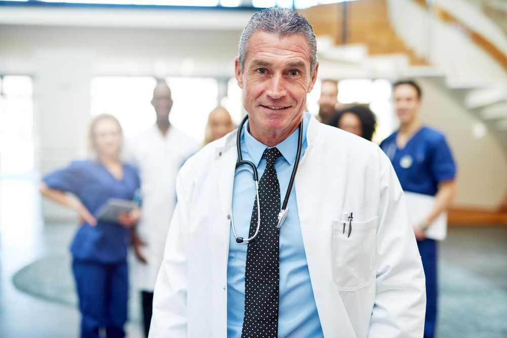 Portrait of mature doctor in lab coat and stethoscope with his medical team in the background