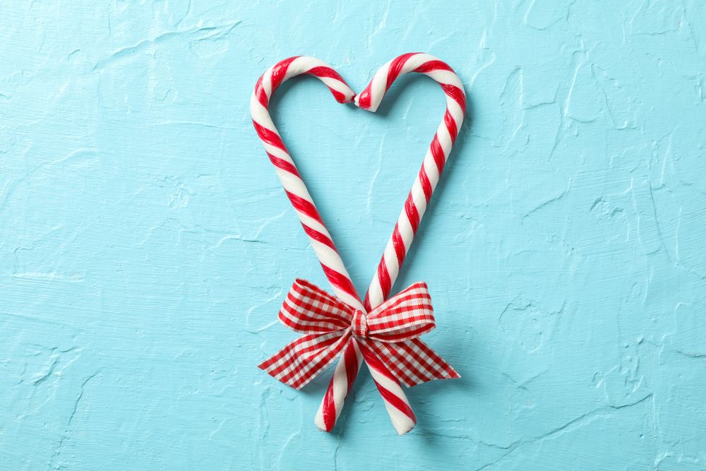Sweet candy canes with bows on blue background, space for text