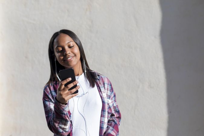 Female standing in the sun in front of wall checking phone
