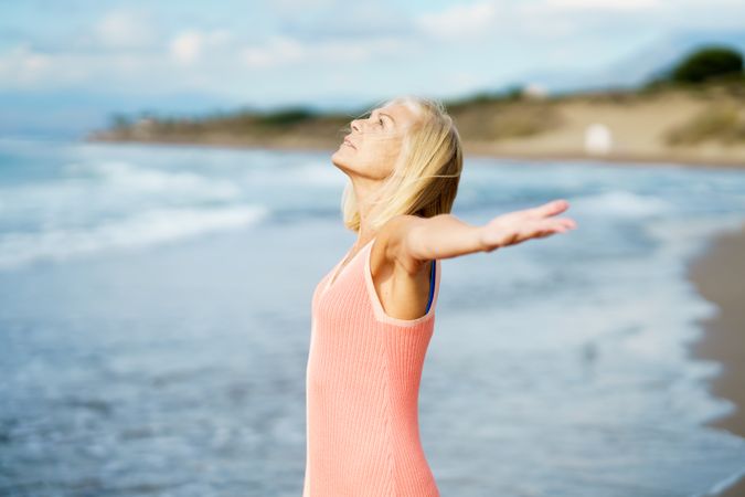 Carefree mature woman standing on the coast with her arms outstretched
