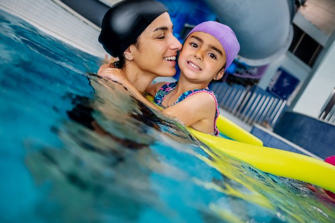 Cheerful girl swimming in pool with mother
