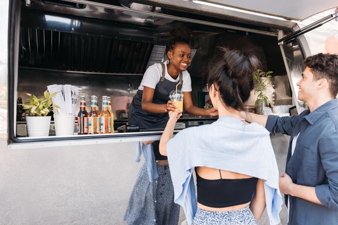 Back of male and male and female customers receiving drinks from saleswoman