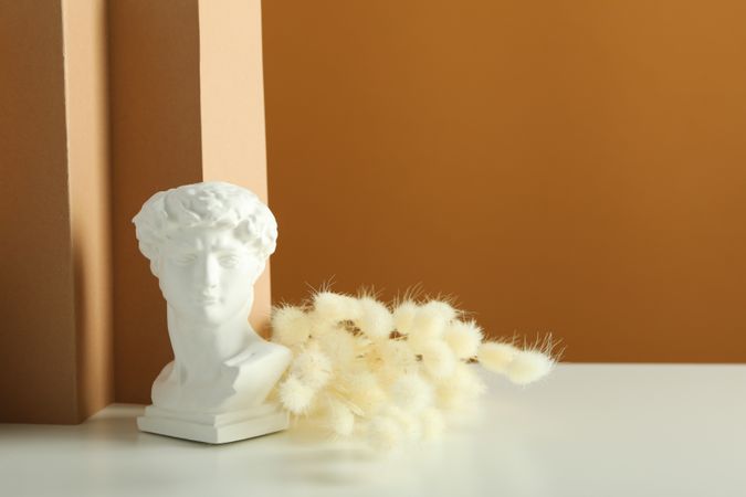 Bust on table with dried flowers in brown room with copy space