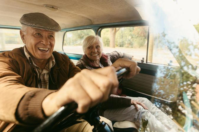 Smiling older man driving a vintage car with his date sitting in passenger seat