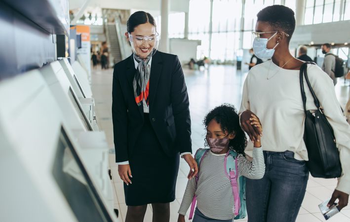 Airlines attendant assisting girl and mother with self service check-in machine