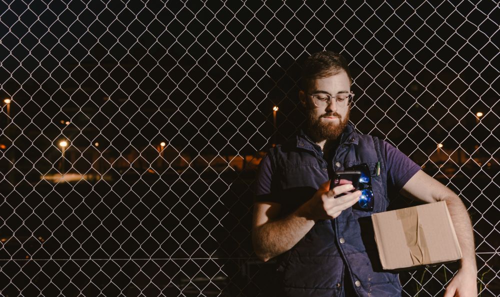 Courier with carton waiting client on street in evening