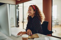 Woman with curly hair smiling at her computer at work