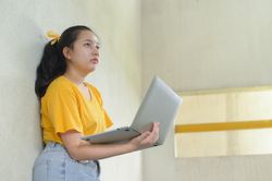 Young woman with laptop standing on a cement wall, work from home.