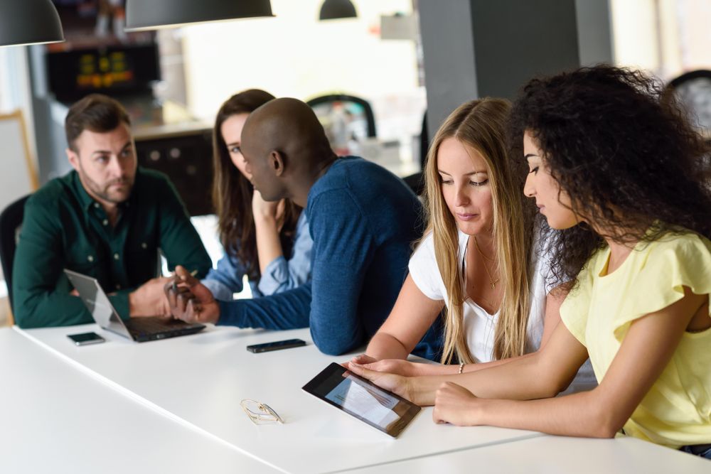 Five male and female colleagues studying with tablet and laptop computer on desk