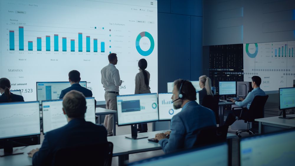 Data Analysts Examine Financial Charts on Large Screen in Modern Office.
