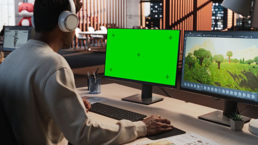 Indian Male Game Designer Using Desktop Computer With Green Screen Chromakey on Display, Designing Immersive World In 3D modelling Software For RPG Video Game.