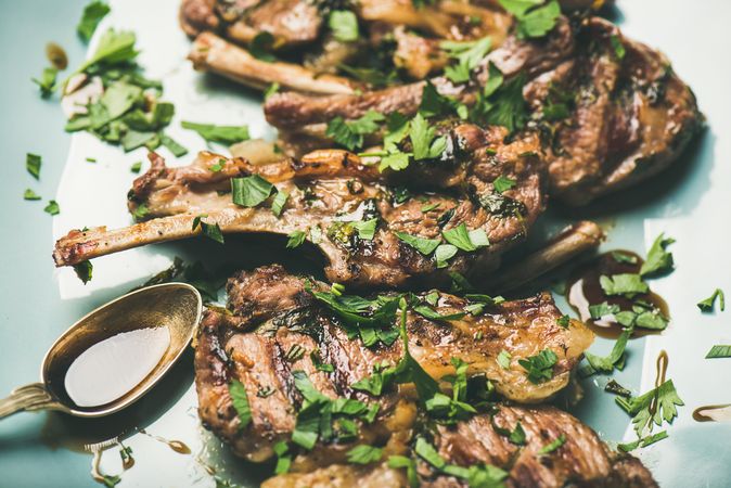 Plate of grilled lamb chops with parsley garnish on light blue plate, close up