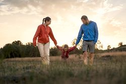 Happy family holding hands and walking together in a field at sunset.