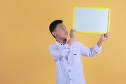 Portrait a young man in yellow backdrop holding a blank note board