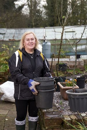 Older woman lifting empty pots in garden, vertical