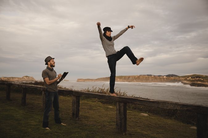 Couple holding hands and jumping on bench on shore near water