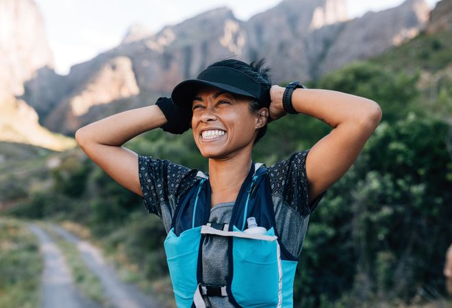 Laughing woman hiker holding cap enjoying the view