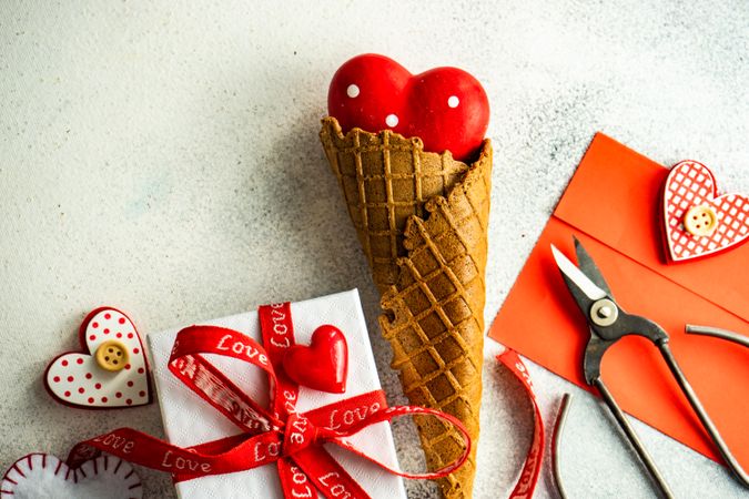 Red heart ornaments in waffle cone with envelope and gift on grey background
