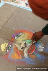 Person drawing face on sidewalk floor with colorful chalks in London, UK  47zEr5