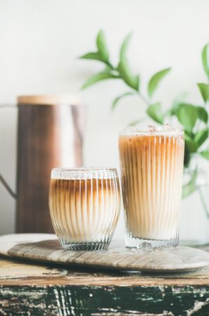 Two glasses of iced coffee, with light background with leaves and pitcher