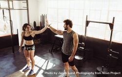 Man and woman standing on box and giving high five at gym bGyVB5