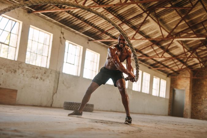 Fitness man exercising with battle rope in abandoned warehouse