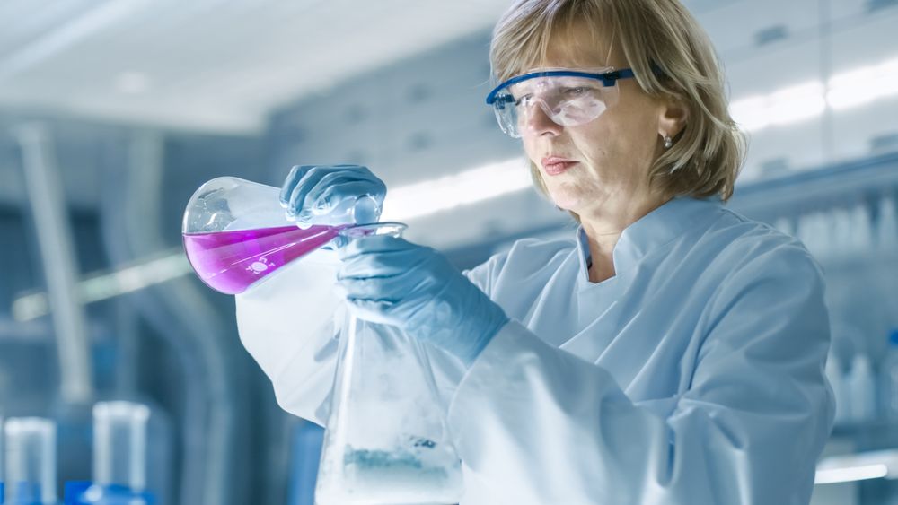 Mature Female Chemist in Safety Glasses Mixes Smoking Liquids in a Beakers.