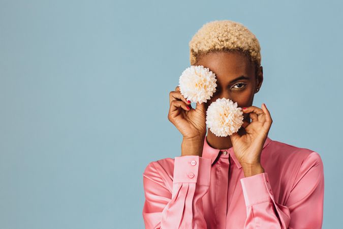 Black woman with short blonde hair holding two flowers over her face