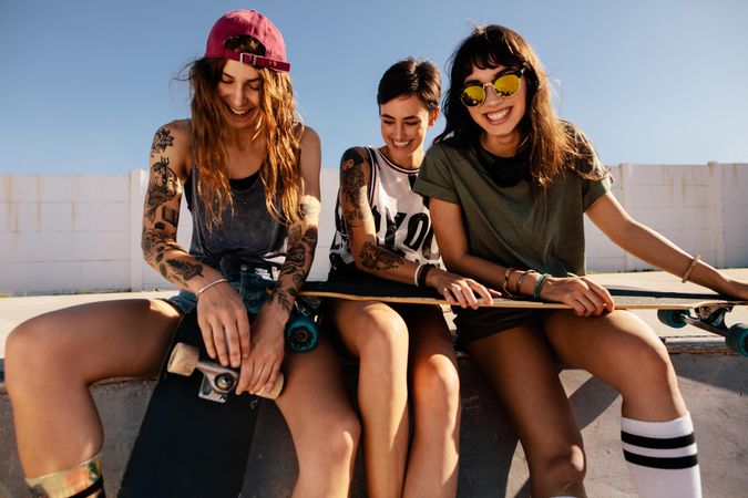 Three women skateboarders sitting together at the top of a skate ramp smiling