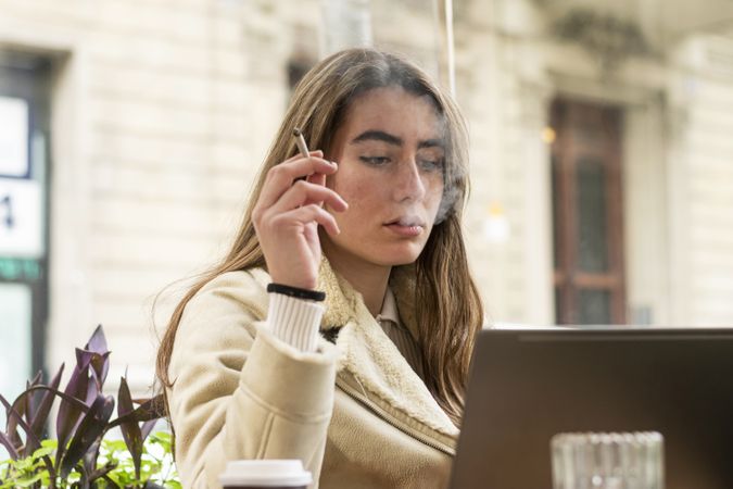 Young brunette using laptop in a cafe with cigarette