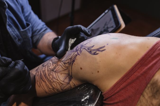 Master doing tattoo on forearm of male customer