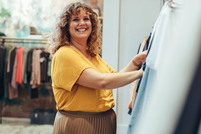 Happy woman looking at clothes on rack in store