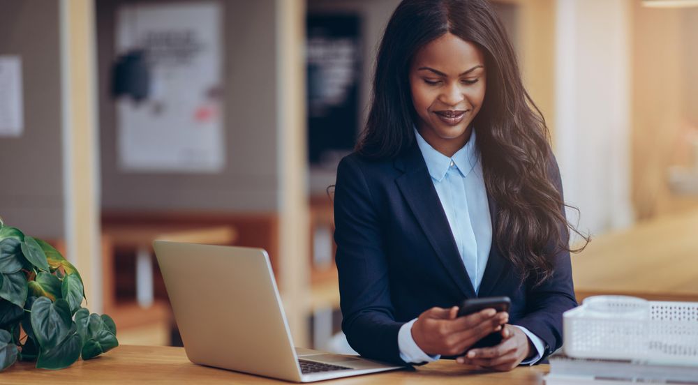Woman texting on a cellphone at a laptop